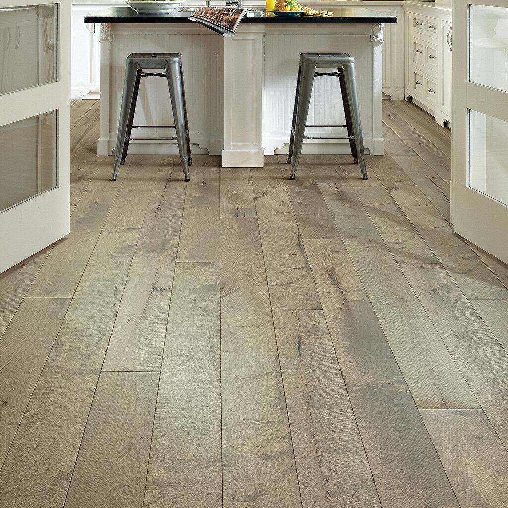 Kitchen island with black stools on light honey-toned traditional hardwood flooring.